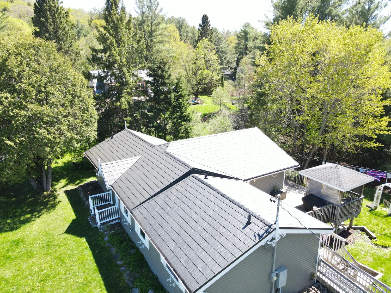 Completed grey metal shingle roof across the intersecting roof planes of a home surrounded by trees