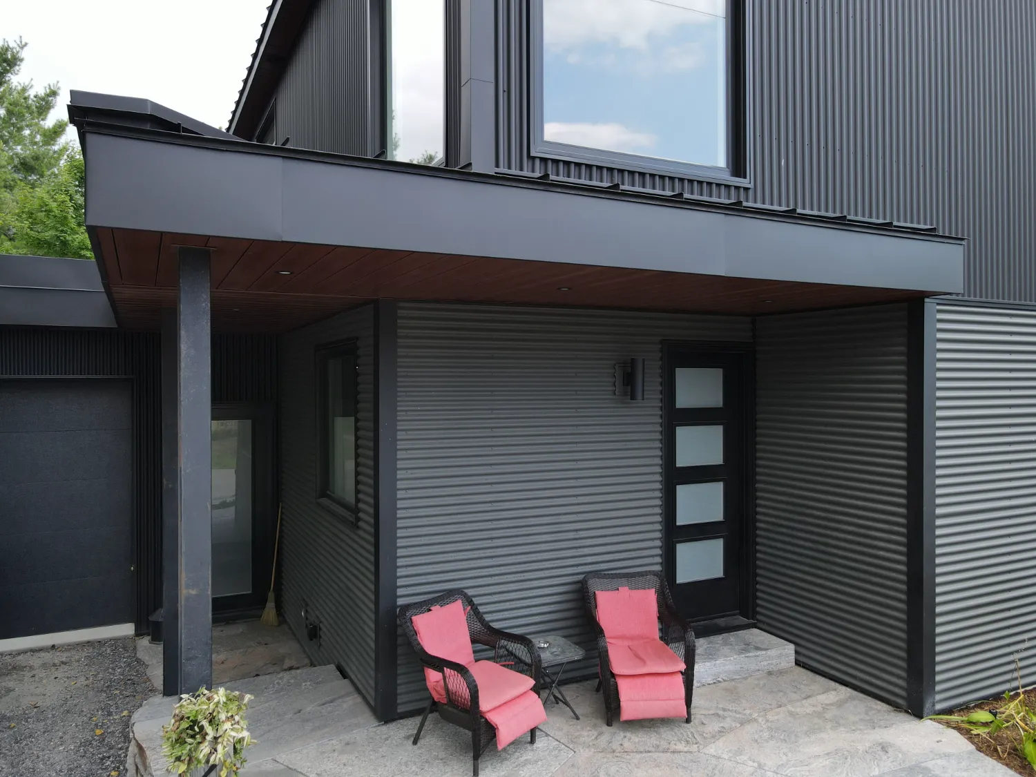Dark corrugated metal siding, a crisp fascia edge and wood-toned soffit around a modern home entrance