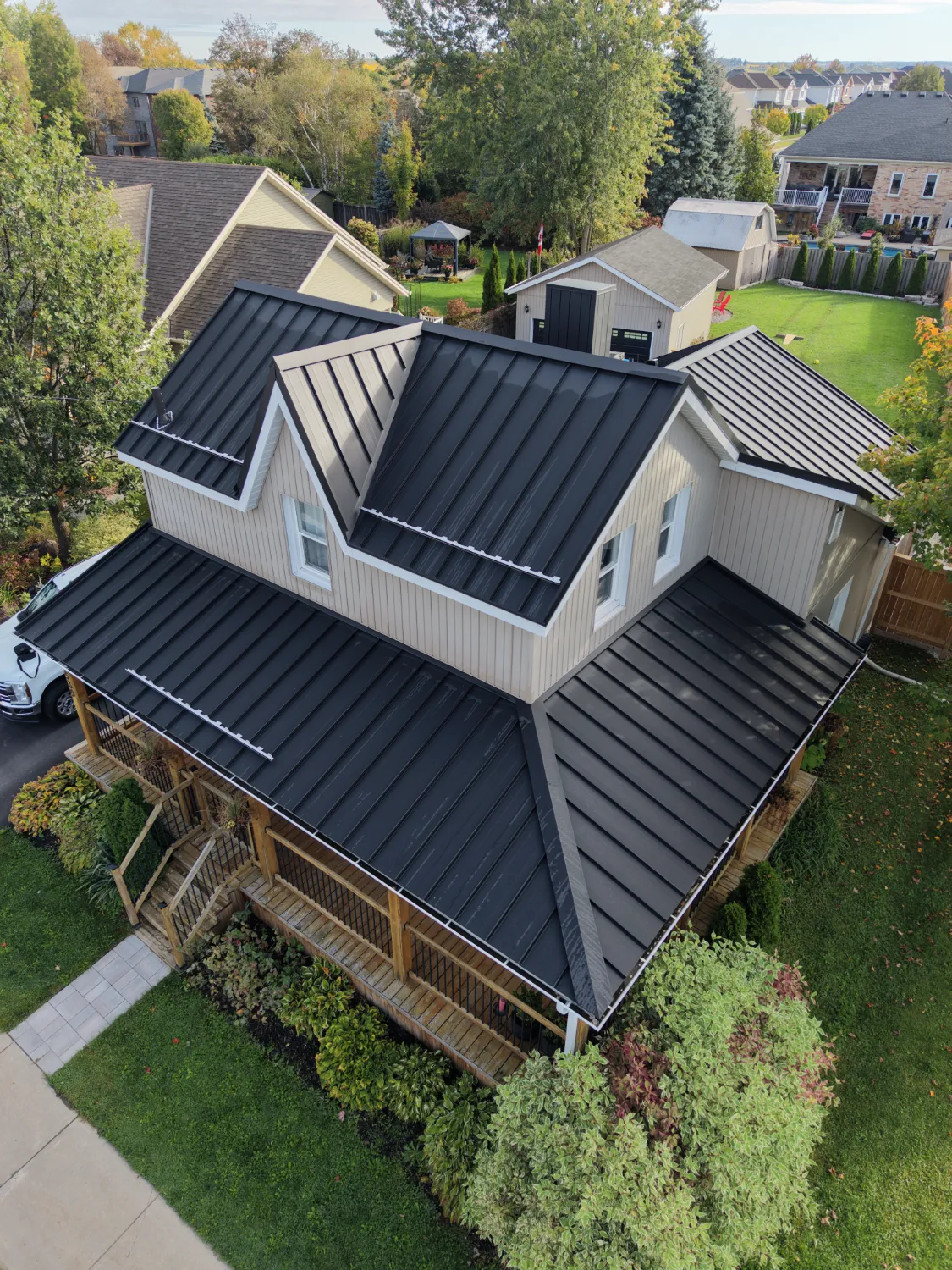 Black standing-seam metal roofing following the dormers and wraparound porch of a light-sided home